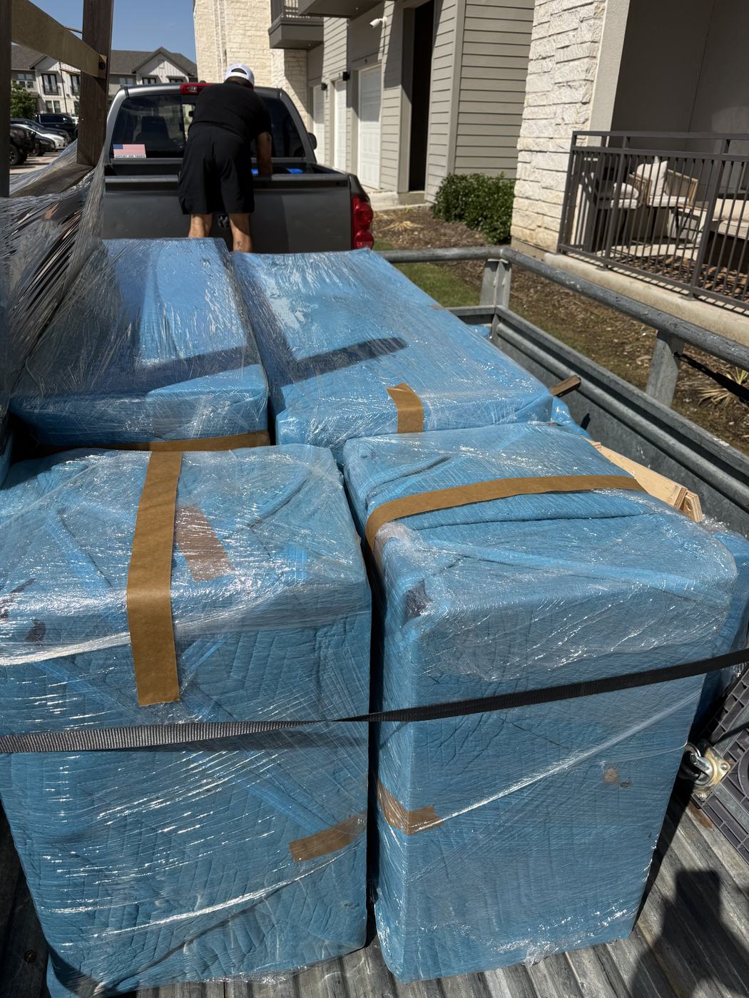 American Outlaw Logistics crew loading blanket-wrapped and strapped furniture onto a trailer at a Fort Worth apartment complex