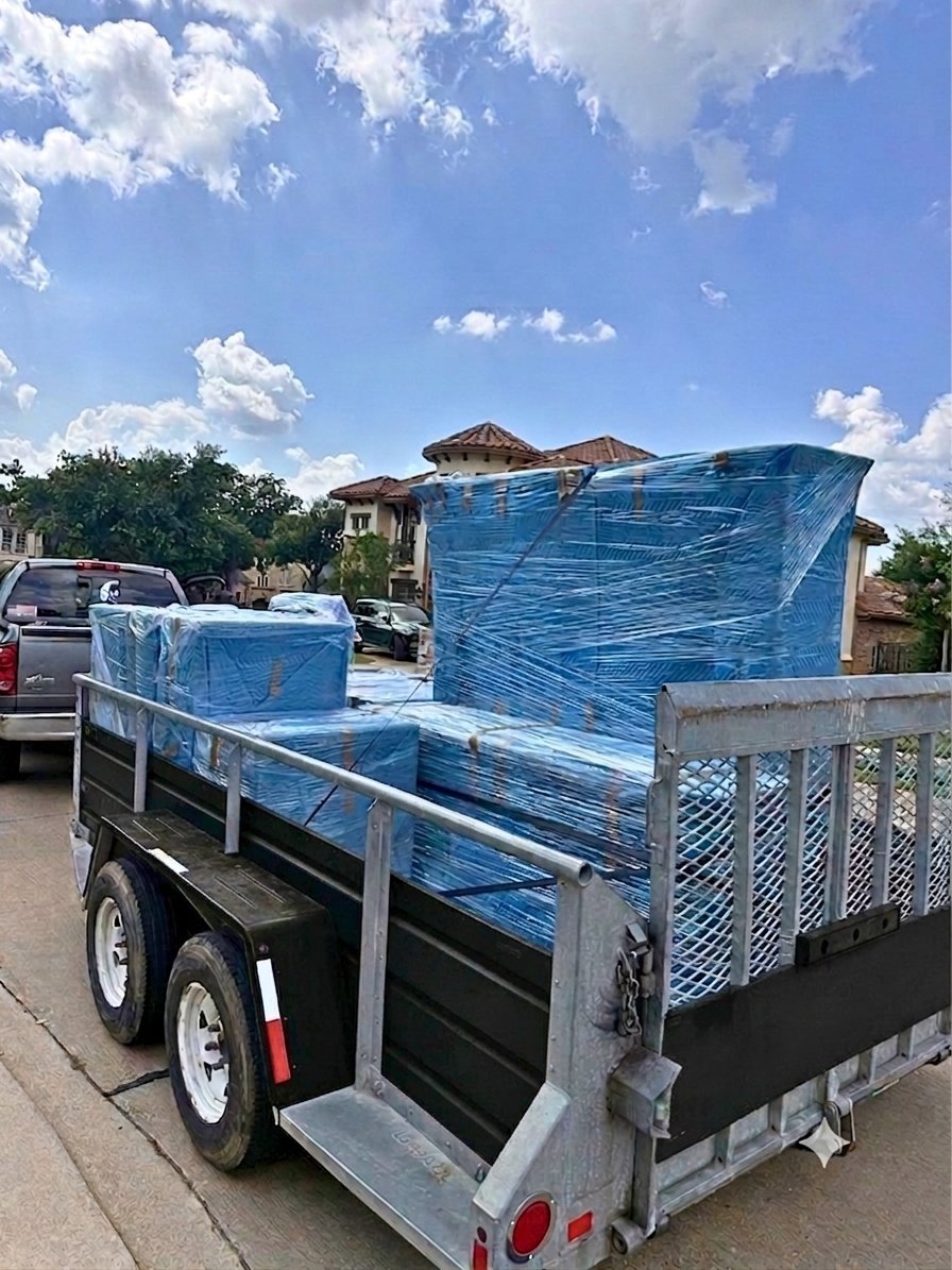 Furniture wrapped and strapped for transport on an American Outlaw Logistics trailer outside a Fort Worth-area home